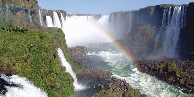 A view of Iguazu Falls, with lush greenery and a rainbow in the mist.