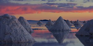 Salt mounds reflected in the water on the Uyuni Salt Flats at sunset, with a colorful sky in the background.