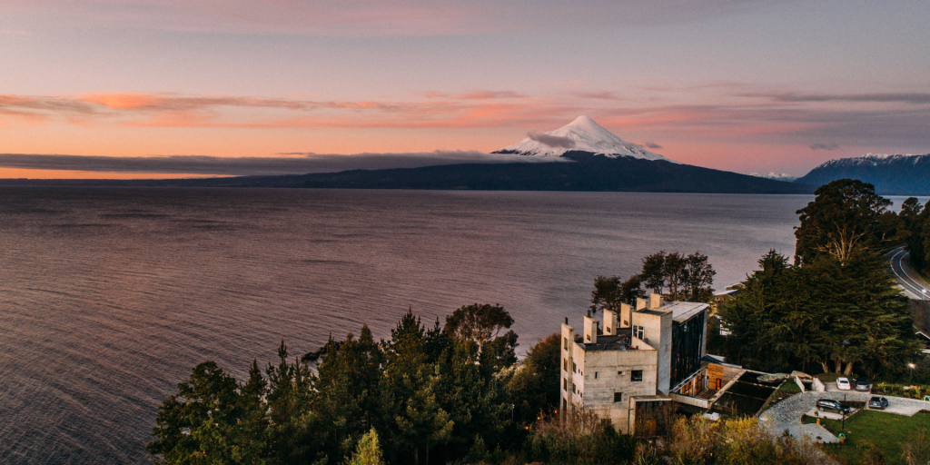 A scenic aerial view of AWA Hotel with a majestic volcano in the background and a calm lake in the foreground.