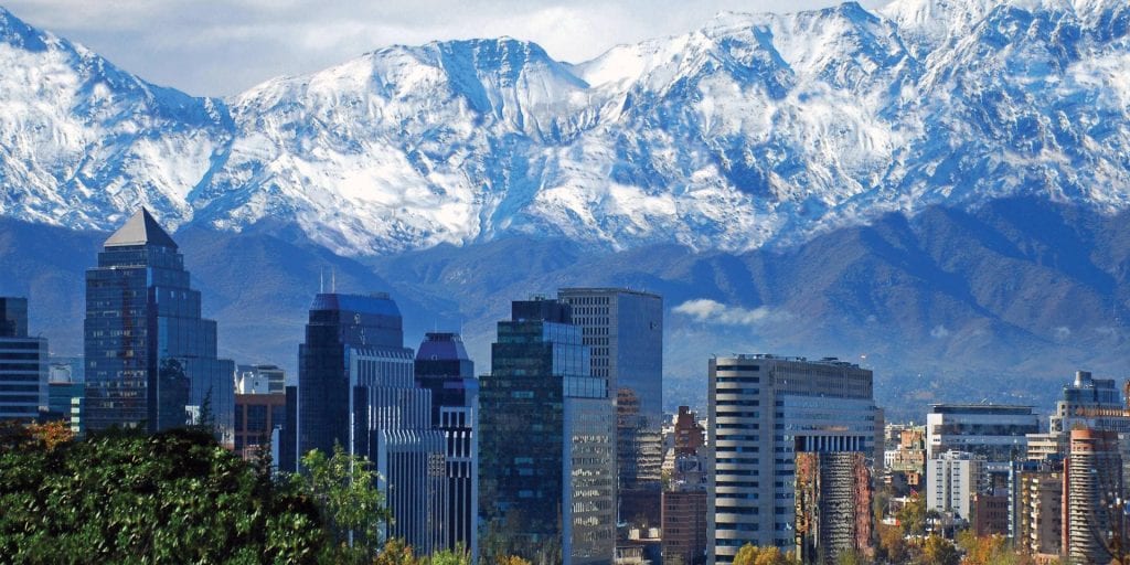 A panoramic view of Santiago, Chile, featuring towering skyscrapers against the backdrop of the Andes Mountains.