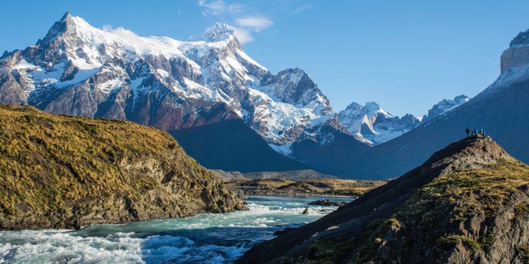 A group of people standing on a rock overlooking a river and mountains in Torres del Paine National Park.