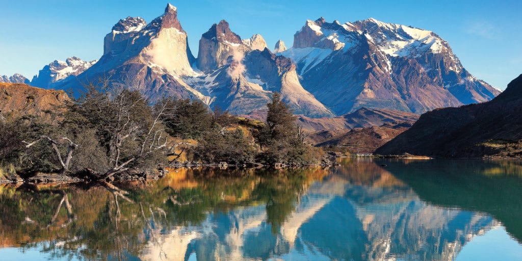 A stunning view of the Torres del Paine mountain range in Patagonia, with a crystal-clear lake in the foreground.
