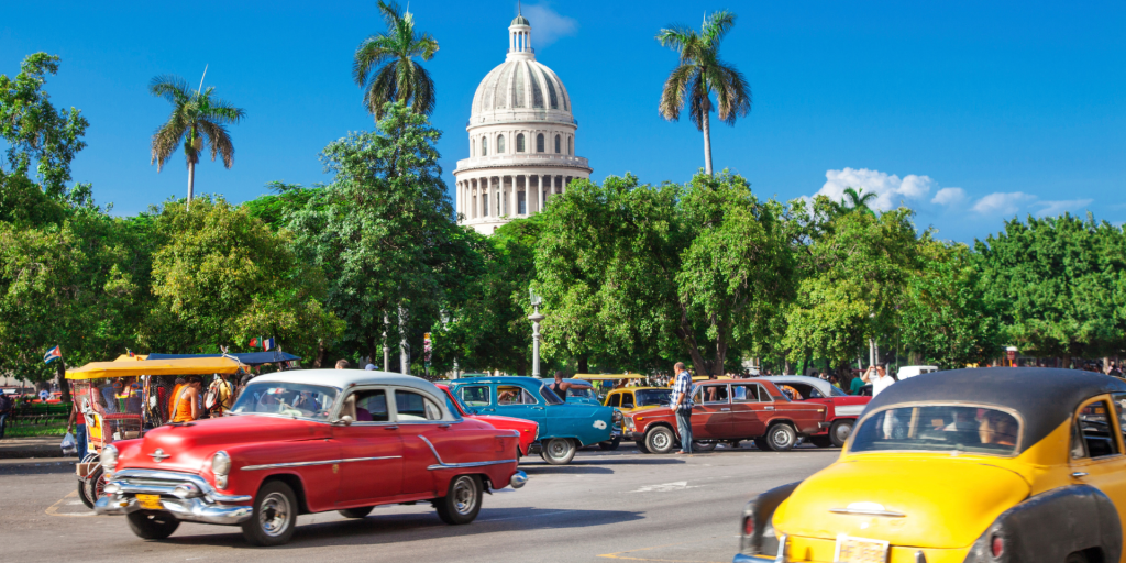 A row of colorful classic American cars parked on a street in Havana, Cuba, with the Capitol building in the background.