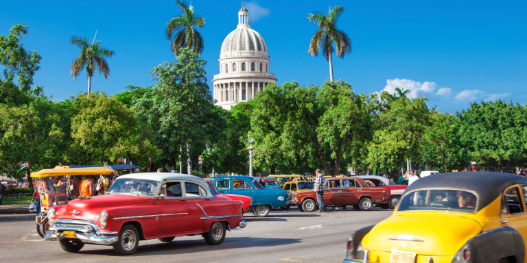 A row of colorful classic American cars parked on a street in Havana, Cuba, with the Capitol building in the background.