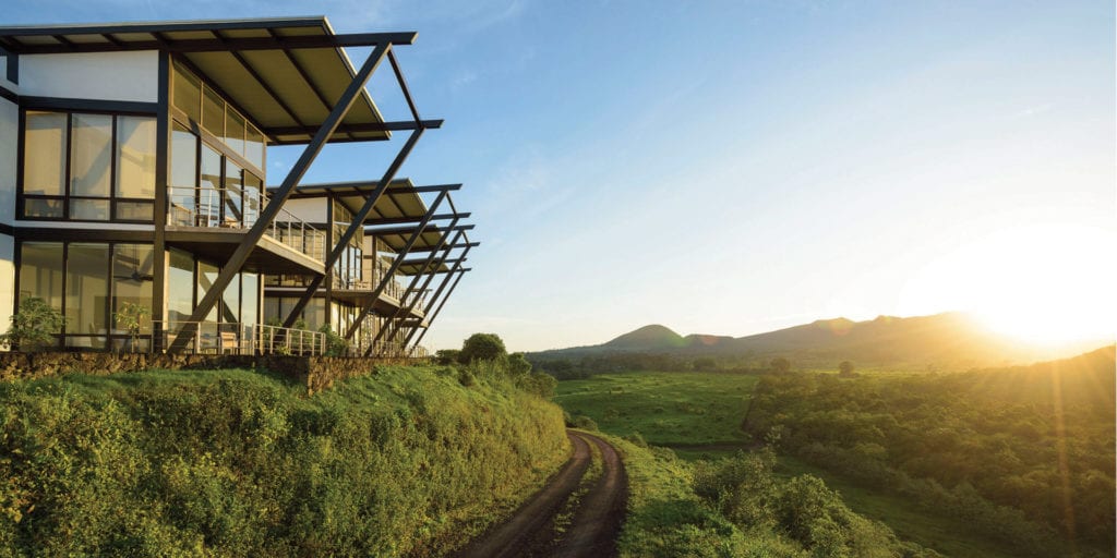 A modern hotel building nestled into a hillside with a stunning view of the Galapagos landscape.