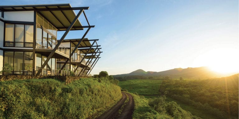 A modern hotel building nestled into a hillside with a stunning view of the Galapagos landscape.