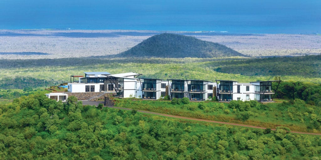 Aerial view of the sustainable luxury Pikaia Lodge situated on a lush green hilltop in the Santa Cruz highlands, Galapagos Islands, featuring modern architecture and a distant ocean view.