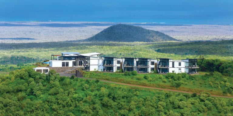 Aerial view of the sustainable luxury Pikaia Lodge situated on a lush green hilltop in the Santa Cruz highlands, Galapagos Islands, featuring modern architecture and a distant ocean view.