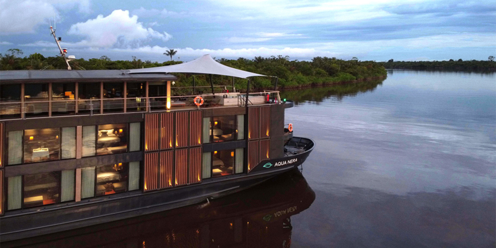 A modern, sleek cruise ship, Aqua Nera, sailing down the Amazon River with lush rainforest in the background.