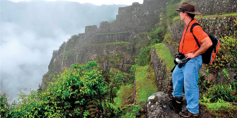 Hikers walking on a trail in the Andes Mountains, with Machu Picchu in the distance.
