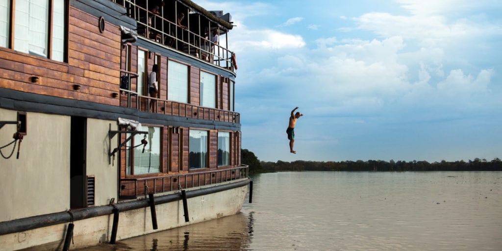The Delfin III Amazon Cruise vessel sailing on the Amazon River under a clear blue sky.