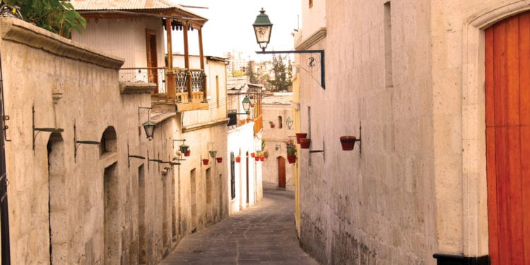 A narrow, sunlit cobblestone street lined with light-colored colonial buildings in Arequipa, Peru