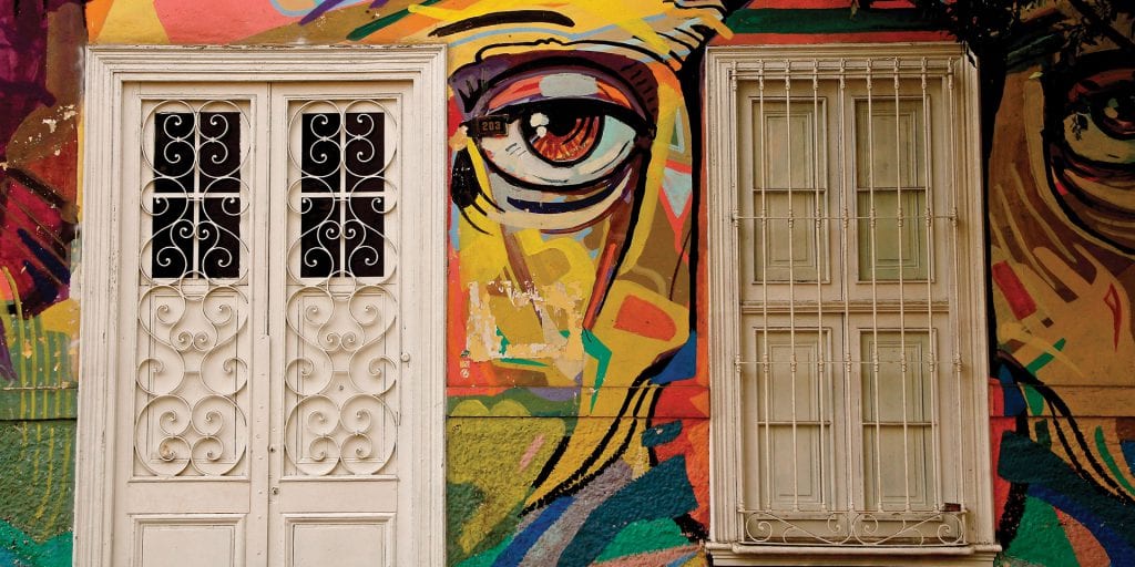 A colourful mural on a building in Barranco, Lima, featuring a large eye, white doors, and a window.