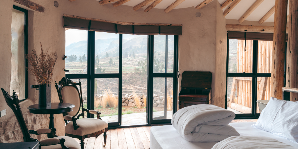 A cosy bedroom in a rustic lodge with large windows overlooking a mountain landscape.