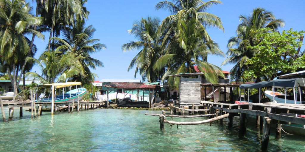 A view of a village on a small island with wooden houses, boats, and palm trees.