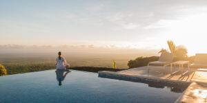 A woman meditating at the edge of an infinity pool overlooking a stunning Galapagos landscape.