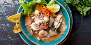 A vibrant bowl of Peruvian ceviche, filled with fresh seafood, red onion, chili peppers, and corn, served with lettuce and fried sweet plantains.