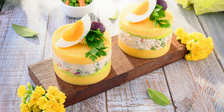 Two layers of mashed yellow potatoes with a filling of tuna, olives, and vegetables, topped with a hard-boiled egg and parsley.