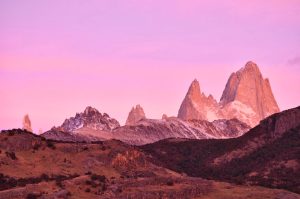 A breathtaking panoramic view of Fitz Roy mountain range bathed in a pink sunset glow.