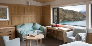 Room with panoramic lake and mountain view at Explora Torres del Paine, including comfortable seating and natural wood finishes.