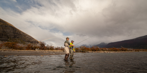 Angler casting a fly rod in a pristine Patagonian river with stunning mountain scenery.