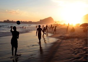A vibrant sunset illuminates Copacabana Beach in Rio de Janeiro, Brazil, as locals enjoy the warm evening.